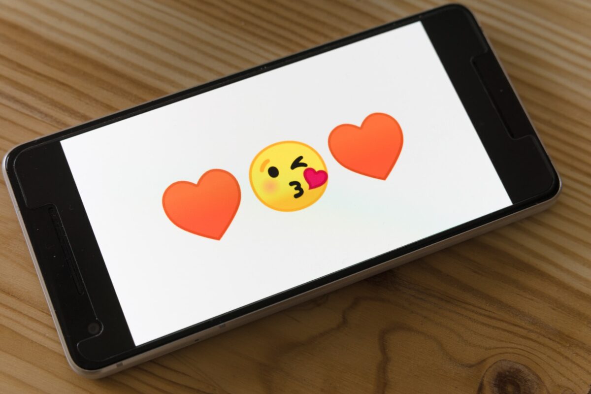 Amor virtual existe? Imagem do celular cuja tela contém um emoji de beijo entre 2 corações
