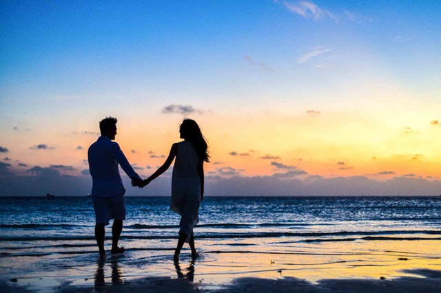 Namoro à distância: casal andando na praia de mãos dadas