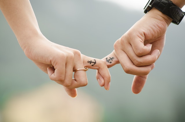 Namoro à distância - casal entrelaçando os dedos, com tatuagens idênticas de âncora